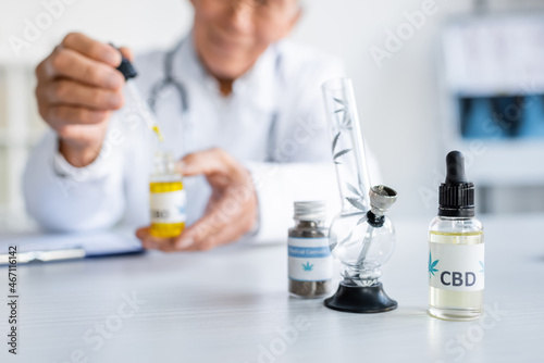 Cropped view of cbd oil and glass bong near blurred doctor in hospital © LIGHTFIELD STUDIOS