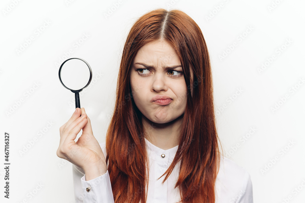 cheerful red-haired woman holding a magnifying glass near her face cheerful red-haired woman holding a magnifying glass near her face