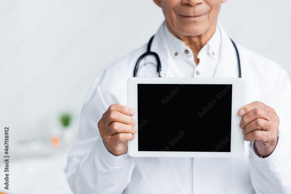 Cropped view of digital tablet with blank screen in hands of blurred doctor in clinic Cropped view of digital tablet with blank screen in hands of blurred doctor in clinic