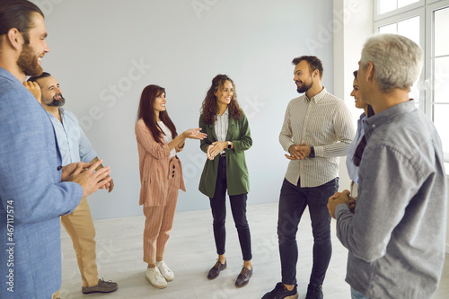 Happy young and mature people having friendly conversation at business event. Group of men and women meeting with business coach. Team of employees standing in office and having interesting discussion