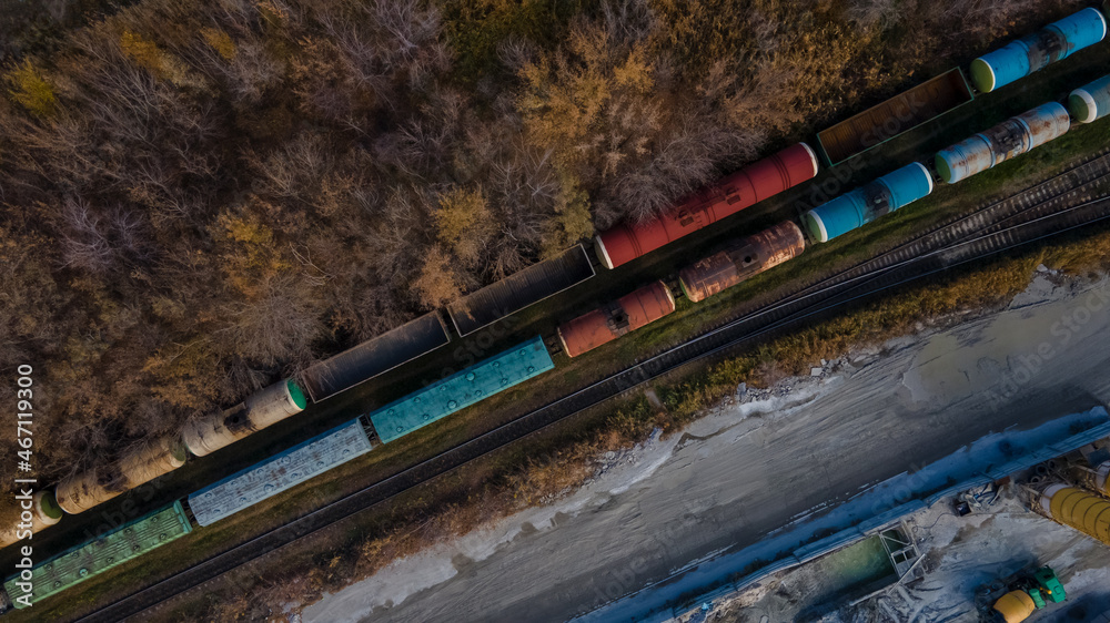 Fototapeta premium Aerial view of railroad in beautiful forest at sunset in autumn. Industrial landscape with railway station, trees with orange leaves in fall. Top view of rural railway platform. Transportation