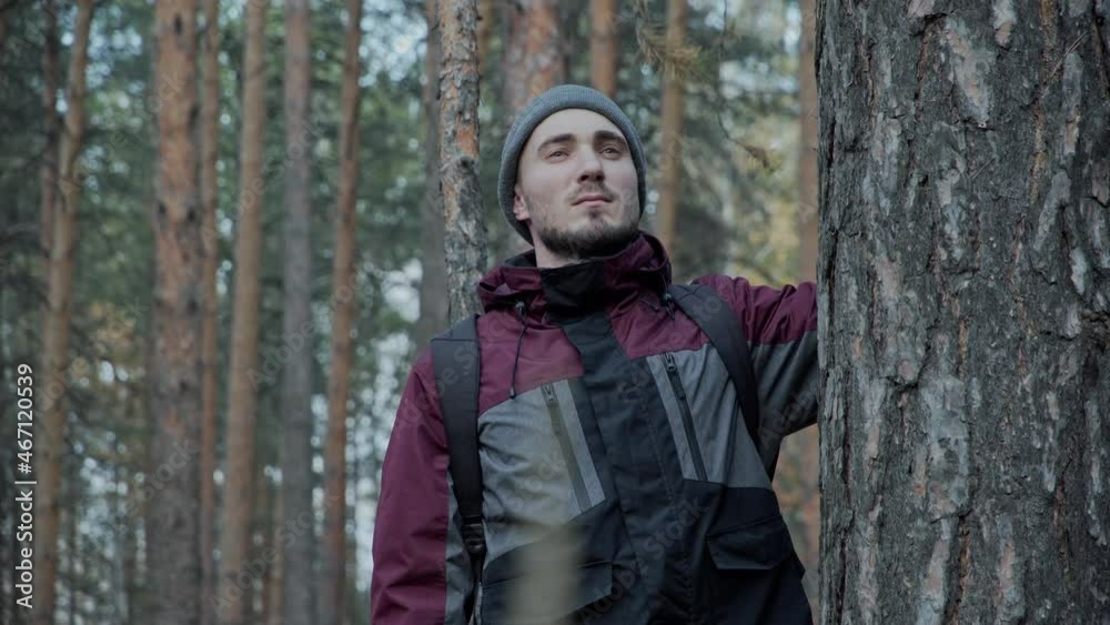 A man in a hat walks through the woods. Portrait of a young male traveler. Forester walking through the forest