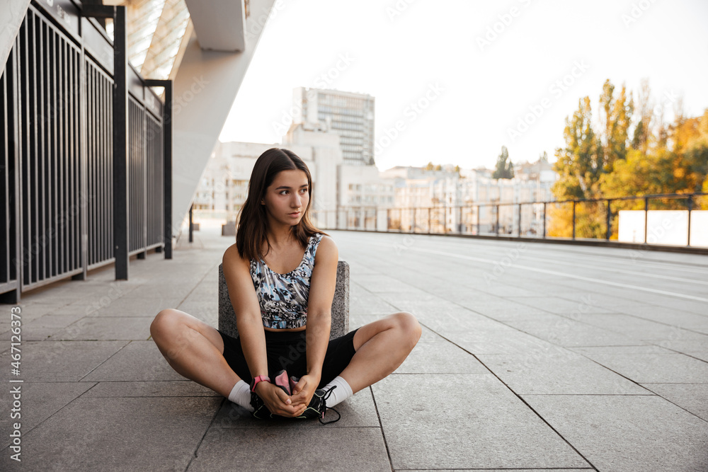 Teenage girl sitting on the floor and resting after training of the city the background Teenage girl sitting on the floor and resting after training of the city the background