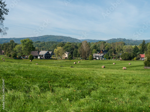 Rural summer landscape with view on village Marenice in Lusitian mountains with traditional wooden cottage and lush green grass meadow, birch deciduous and spruce tree forest and hills, blue sky photo