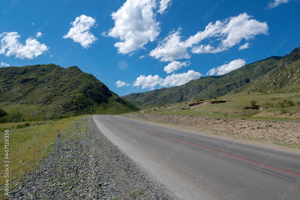 peaks of mountains against the sky with white clouds. Summer sunny day. Mountain asphalt road