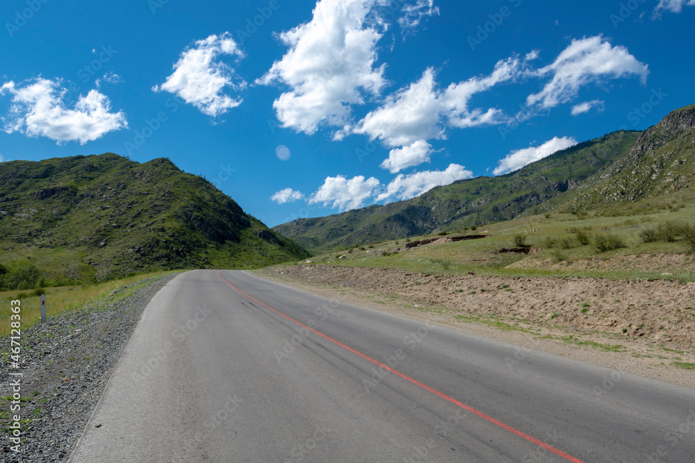 peaks of mountains against the sky with white clouds. Summer sunny day. Mountain asphalt road peaks of mountains against the sky with white clouds. Summer sunny day. Mountain asphalt road