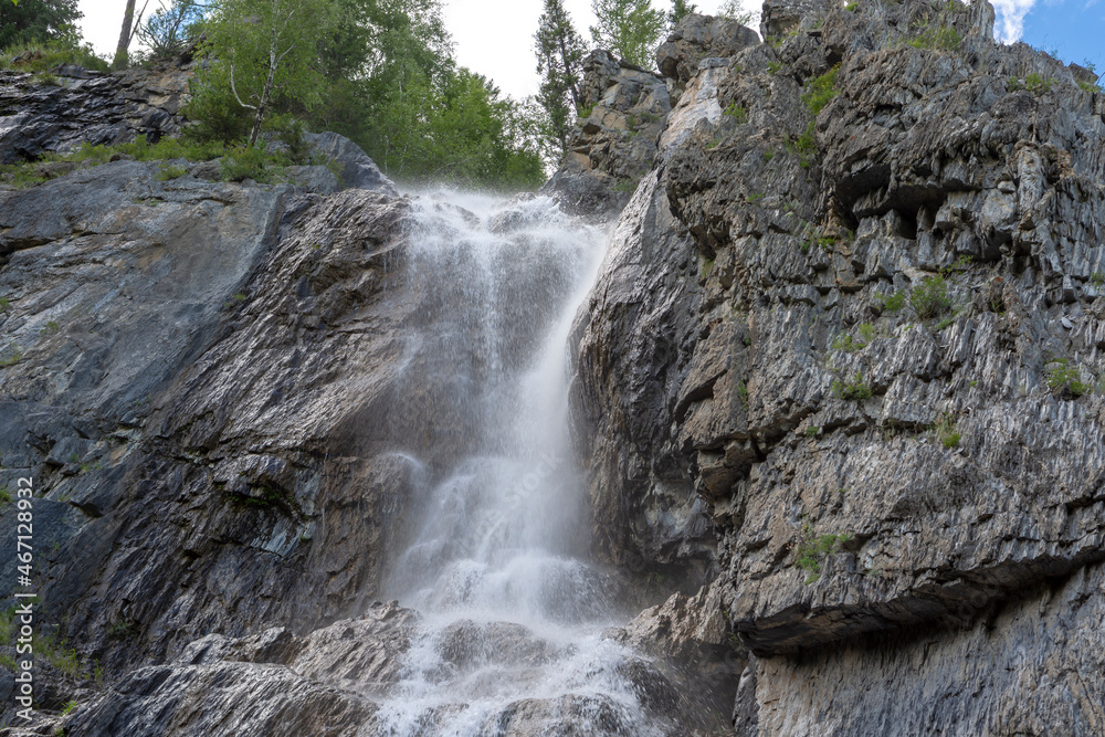 Obraz premium high waterfall on a small river among rocks and green trees