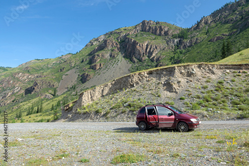 passenger red car parked on a mountain road among small rocks. Summer clear day