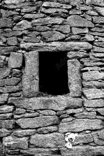 Wall of rustic house at small stone with black hole window