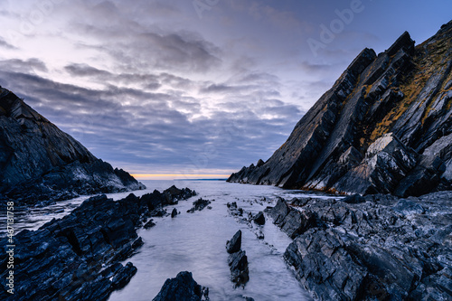Severe rocky coastline of the Barents Sea at sunrise. Beautiful views of the rocks and coast, cold atmosphere. Rybachy Peninsula, Murmansk Oblast, Russia.