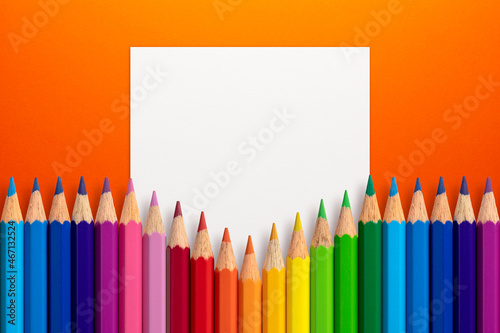 Creative layout made of color pencils on orange paper background with white paper card note. Flat lay. Education concept.