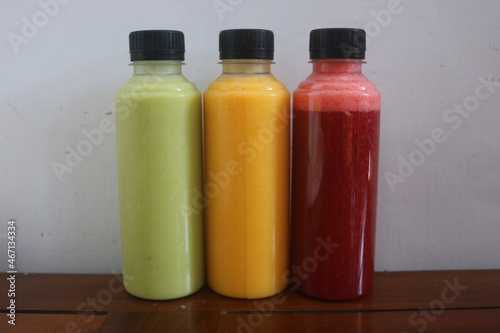 Avocado, mango, strawberry juice served in plastic bottles with black lids

