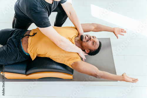 Young fit african american man is concentrated on exercise on pilates reformer bed with male instructor at gym. Sports equipment. Active and healthy lifestyle rehabilitation concept.