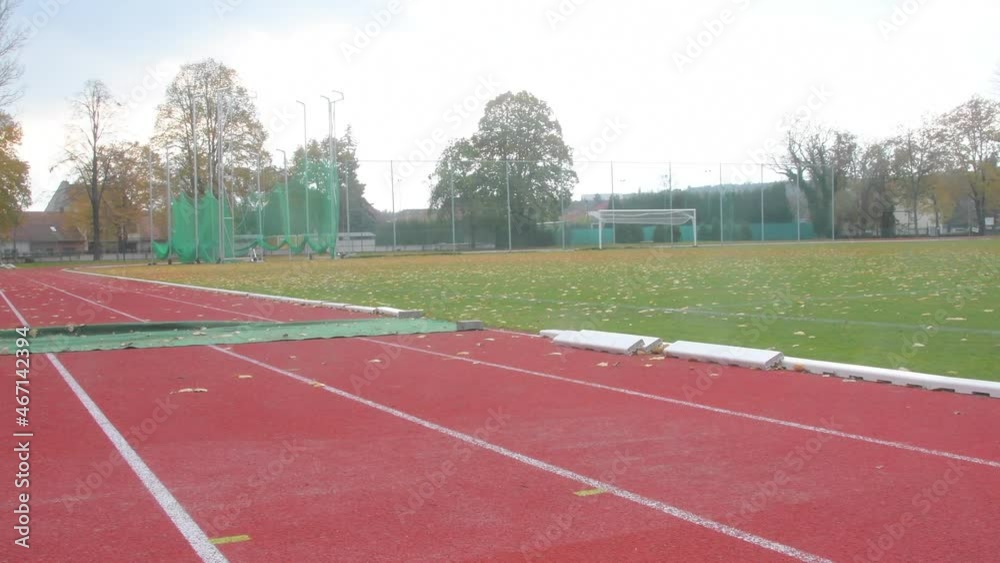 Red running track on athletic stadium in fall. Abandoned athletics track in autumn. Panoramic view on fooball field. Concept of finished athletics and football season