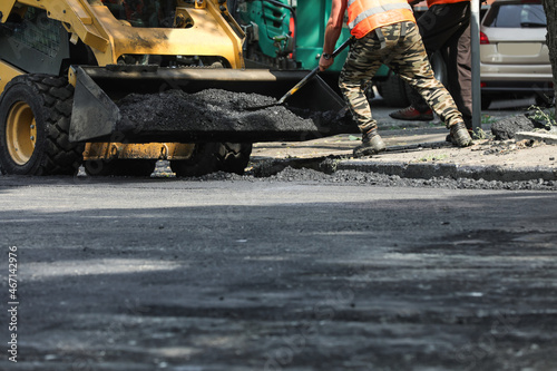 Worker laying new asphalt with skid loader on city street, closeup. Road repair service photo