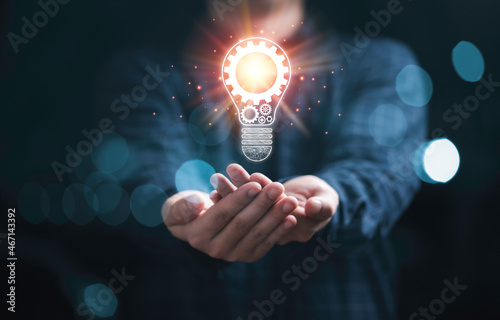 Businessman holding glowing light bulb with mechanical gear and orange light ray for inspiration creative thinking idea and future innovation technology concept.