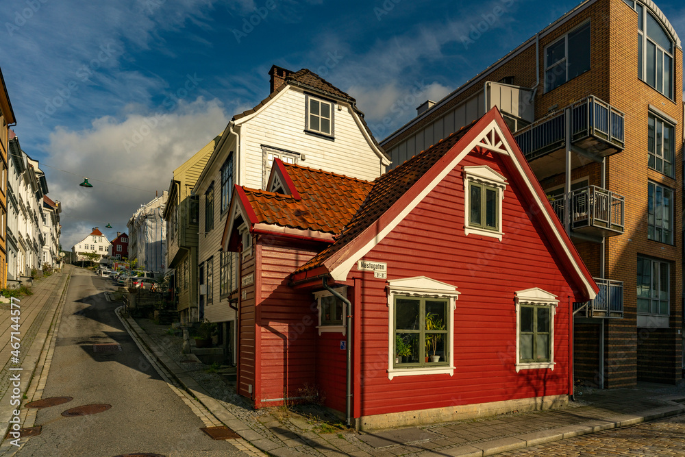 kleines, altes rotes Haus mit weissen Fensterrahmen in Bergen, Norwegen, das zwischen grossen neueren Häusern in der Altstadt steht. herziges, echt nordisches Häuschen mit Stil. norwegischer Flair kleines, altes rotes Haus mit weissen Fensterrahmen in Bergen, Norwegen, das zwischen grossen neueren Häusern in der Altstadt steht. herziges, echt nordisches Häuschen mit Stil. norwegischer Flair
