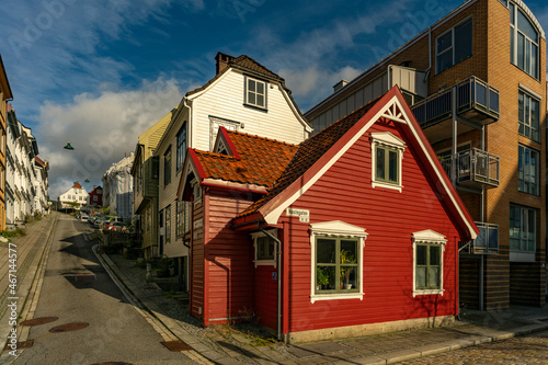 kleines, altes rotes Haus mit weissen Fensterrahmen in Bergen, Norwegen, das zwischen grossen neueren Häusern in der Altstadt steht. herziges, echt nordisches Häuschen mit Stil. norwegischer Flair 