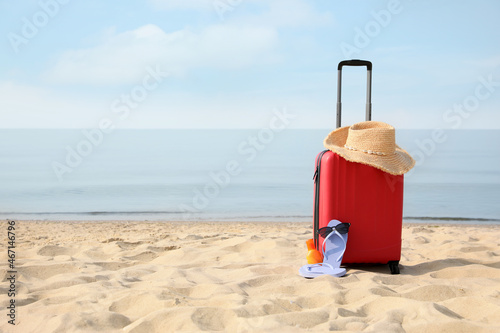 Red suitcase with beach items on sandy seashore  space for text