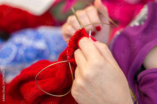 Woman knits with knitting needles red sweater from natural woolen threads