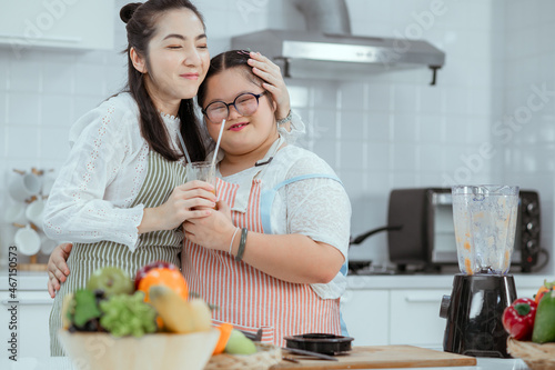 Down syndrome girl makes fruit smoothies in the kitchen at home with mom