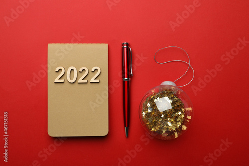 Stylish planner, pen and Christmas ball on red background, flat lay. Planning for 2022 New Year