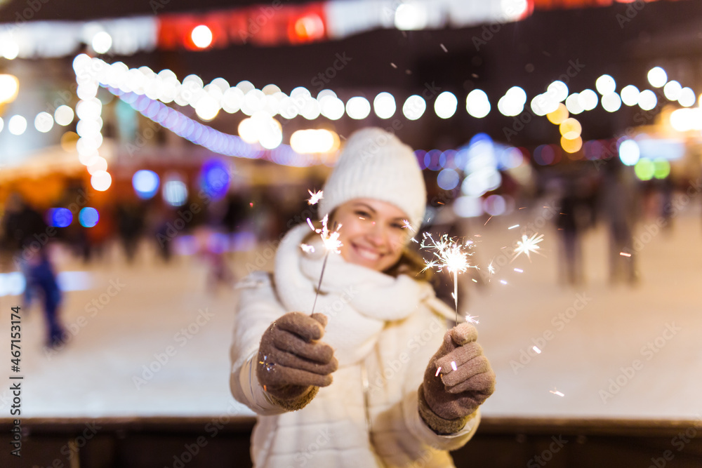 Girl holding a sparkler in her hand. Outdoor winter city background, snow, snowflakes.