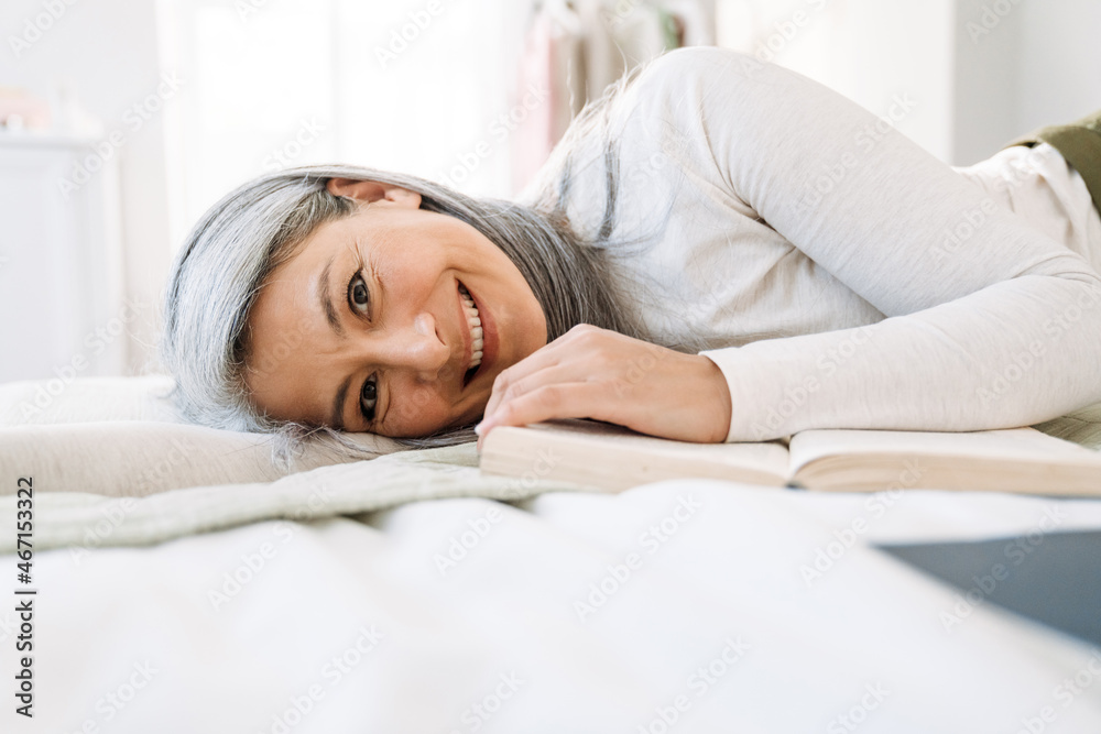 Grey asian woman smiling and reading book while lying on bed Grey asian woman smiling and reading book while lying on bed