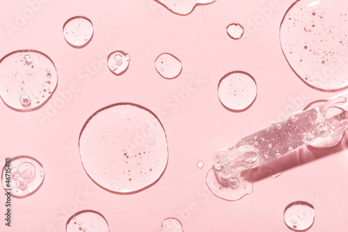 Drops of anti-aging emulsion and glass pipette tip on light pink surface close upper view. Skincare and dermatological procedures