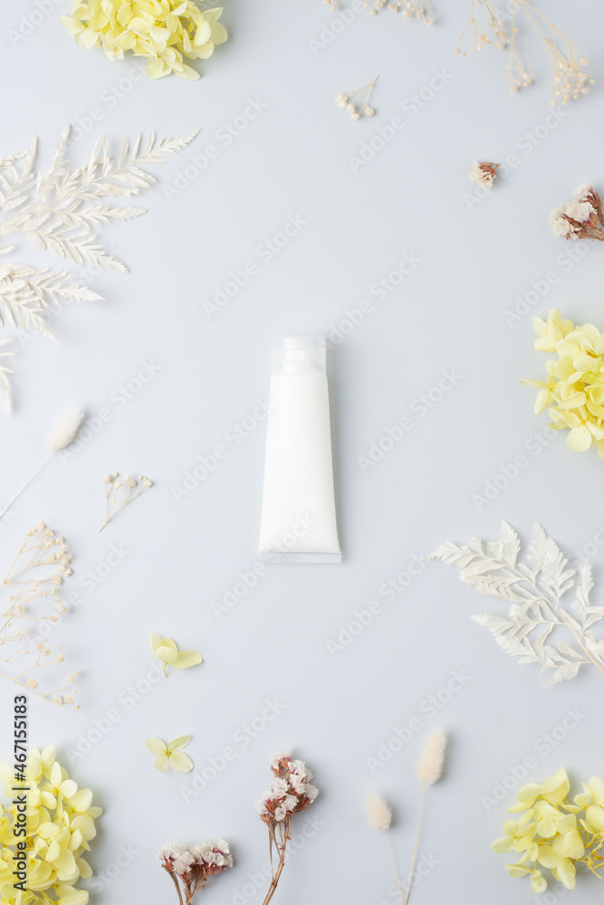 White tube of cosmetic cream with flowers on grey background. Flat lay