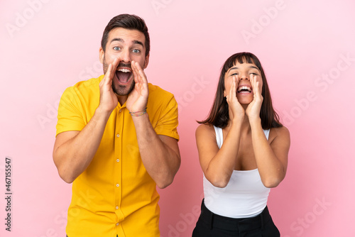 Young couple isolated on pink background shouting and announcing something