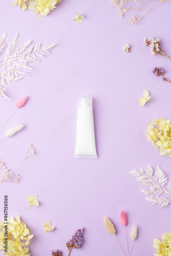 White tube of cosmetic cream with flowers on rose background. Flat lay