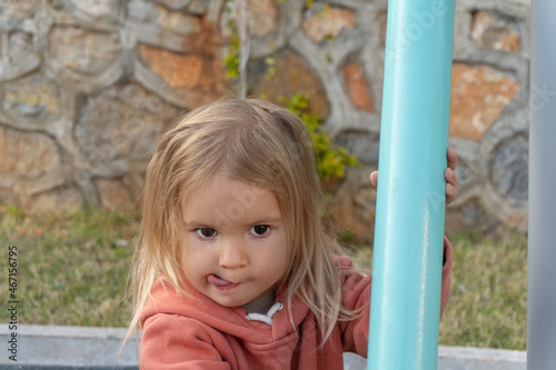 Portrait of cute caucasian little girl looking with curiosity with tongue  child face with emotions  summertime  outdoor activity at playground. 