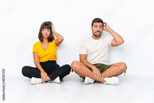 Young couple sitting on the floor isolated on white background takes hands on head because has migraine
