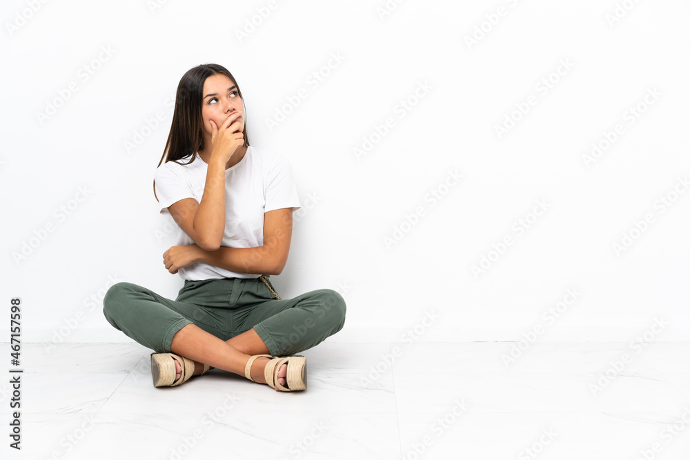 Teenager girl sitting on the floor having doubts and with confuse face expression Teenager girl sitting on the floor having doubts and with confuse face expression