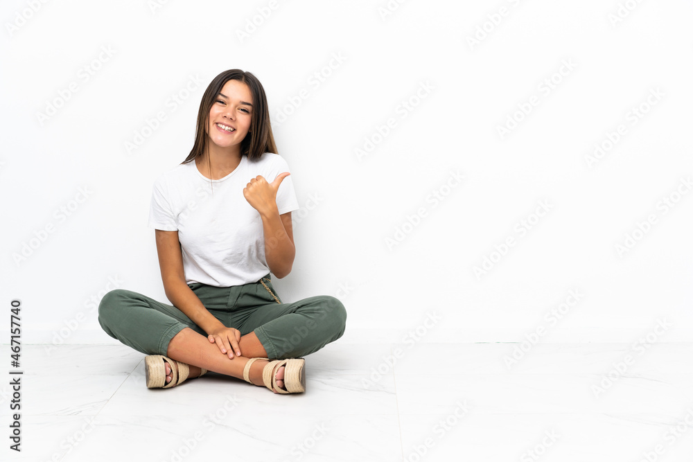 Teenager girl sitting on the floor pointing to the side to present a product Teenager girl sitting on the floor pointing to the side to present a product