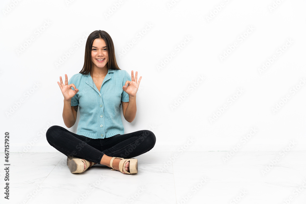 Teenager girl sitting on the floor showing an ok sign with fingers Teenager girl sitting on the floor showing an ok sign with fingers
