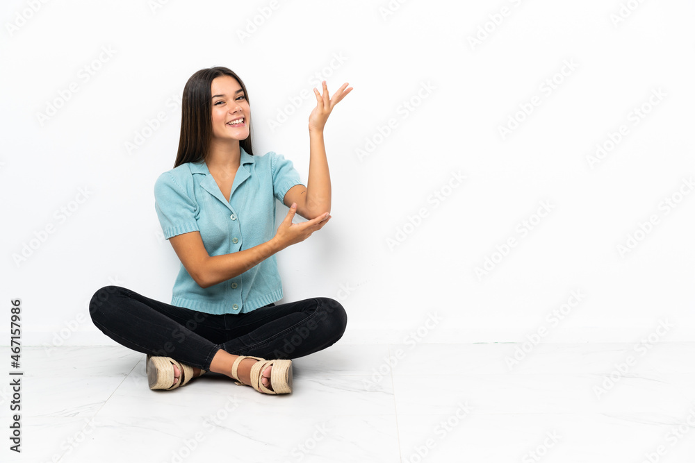 Teenager girl sitting on the floor extending hands to the side for inviting to come Teenager girl sitting on the floor extending hands to the side for inviting to come
