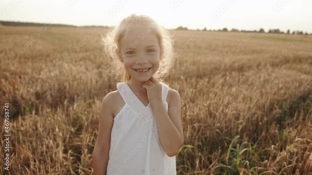 A cheerful preschool girl with a missing front tooth stands in a wheat field and grimaces in front of the camera. Slow motion A cheerful preschool girl with a missing front tooth stands in a wheat field and grimaces in front of the camera. Slow motion