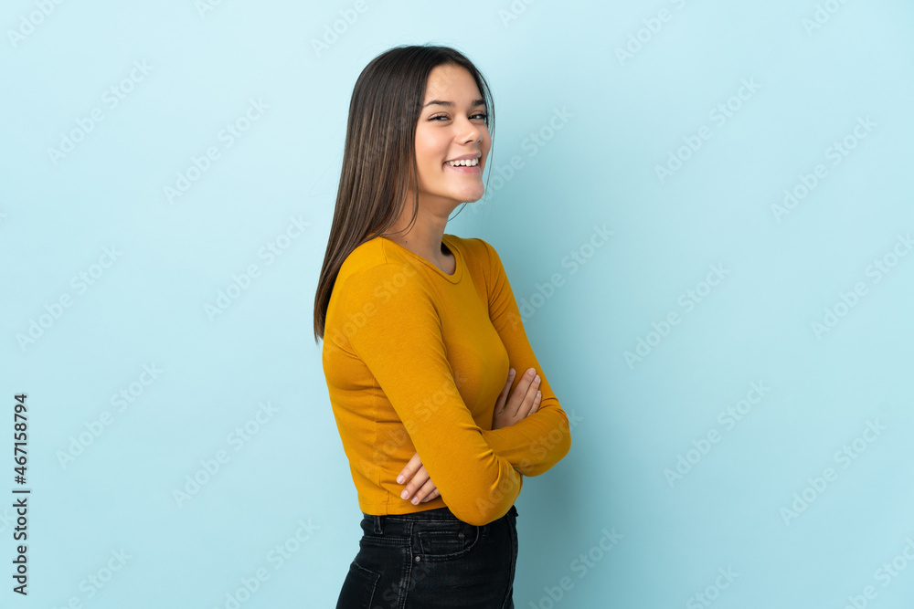 Teenager girl isolated on blue background with arms crossed and looking forward