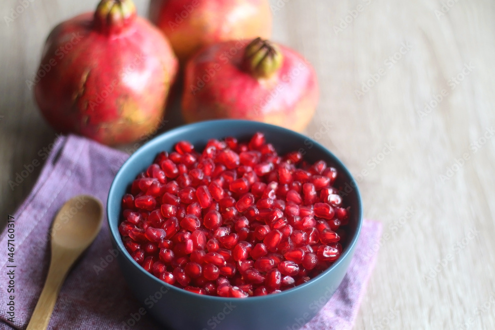 Bowl filled with pomegranate seeds and pomegranate fruit on a table. Selective focus.