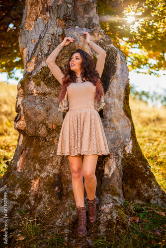 a beautiful woman posing on a log of an old tree in autumn, the colors of autumn