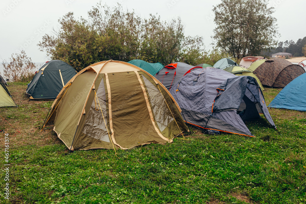  Parking for tents. A tent camp. A cloudy summer day. Tourist meeting. Tents on the river bank. Green grass, gray sky.