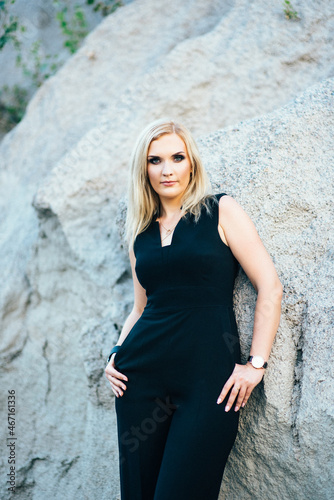 blonde girl in a black trouser suit with blue eyes on the background of a granite quarry