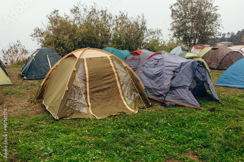  Parking for tents. A tent camp. A cloudy summer day. Tourist meeting. Tents on the river bank. Green grass, gray sky. © Anya