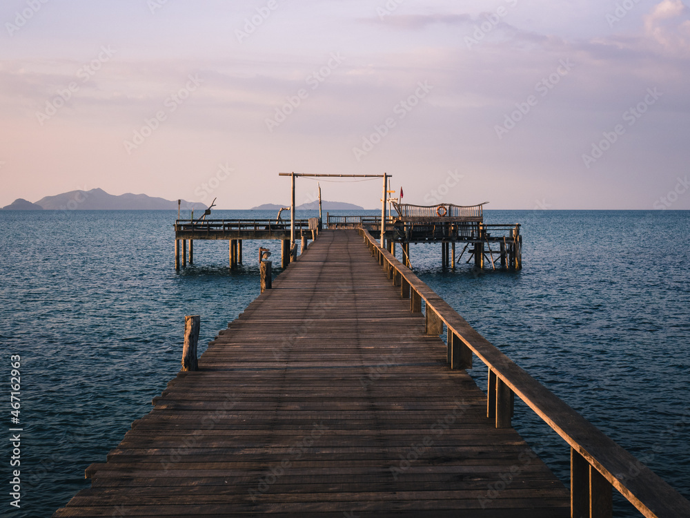 Scenic view of peaceful long straight wooden pier over blue water in evening before sunset. Koh Mak Island, Trat, Thailand. Minimal background. Scenic view of peaceful long straight wooden pier over blue water in evening before sunset. Koh Mak Island, Trat, Thailand. Minimal background.