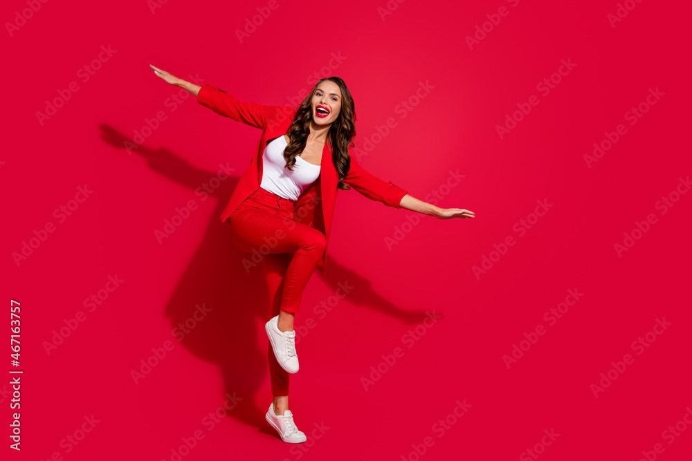 Photo of pretty childish young woman wear suit jacket smiling showing arms plane empty space isolated red color background Photo of pretty childish young woman wear suit jacket smiling showing arms plane empty space isolated red color background