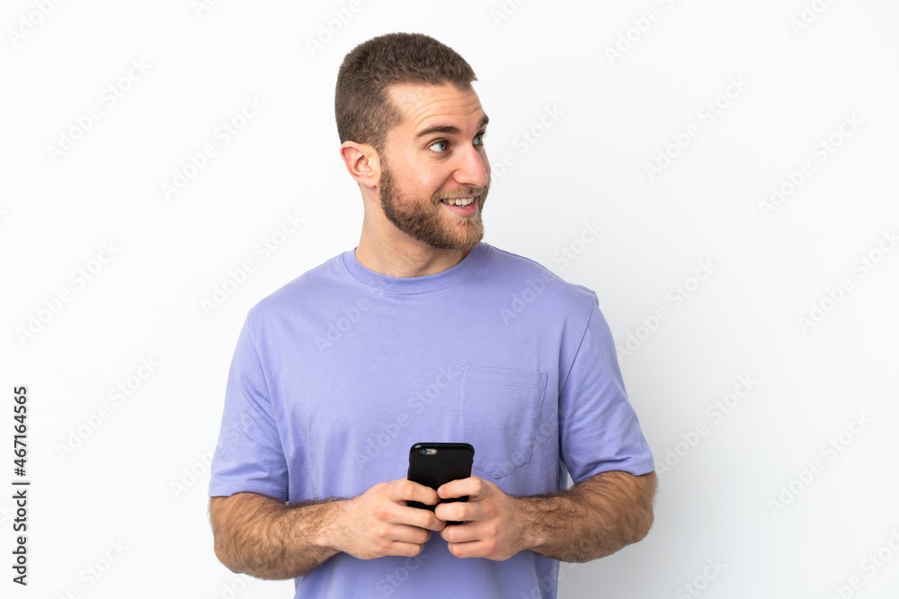 Young handsome caucasian man isolated on white background using mobile phone and looking up