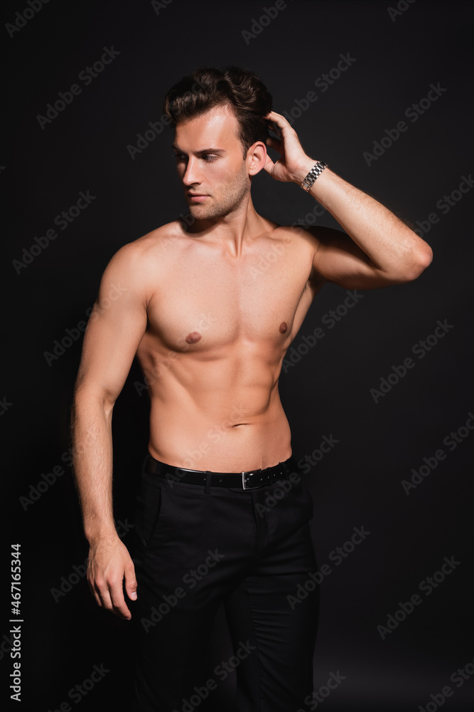 Fototapeta premium young shirtless man with muscular torso holding hand near head while posing on black