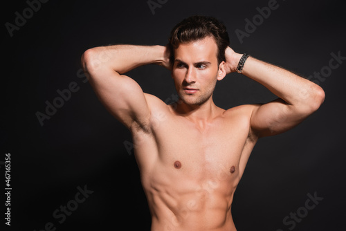 sexy shirtless man with muscular torso posing with hands behind head isolated on black